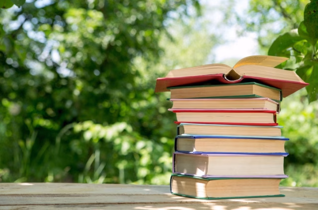 Open book on a wooden table in a garden, sunny summer day, reading in a vacation concept